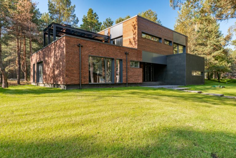 Contemporary brick house featuring large glass windows surrounded by lush green lawn.